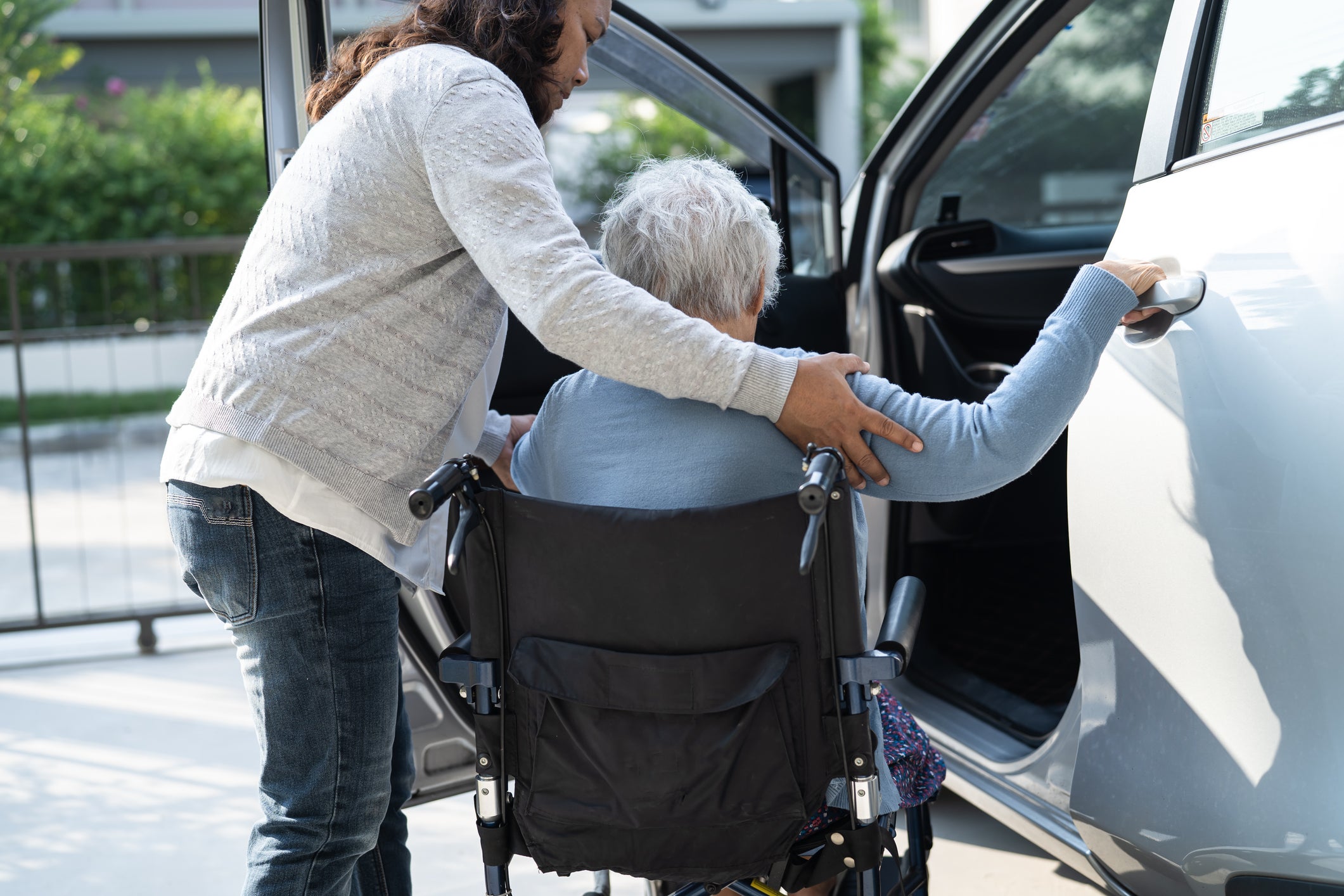 Woman helps elderly lady in wheelchair into vehicle